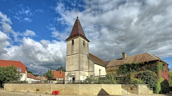 Une photographie aérienne ou grand angle du village de Dannemarie-sur-Crête montrant le paysage vallonné du Doubs avec des maisons de pierre traditionnelles, une église campanile, et l'environnement rural caractéristique de la région. La photo doit être prise de jour avec une bonne luminosité et montrer clairement les éléments architecturaux typiques du village.