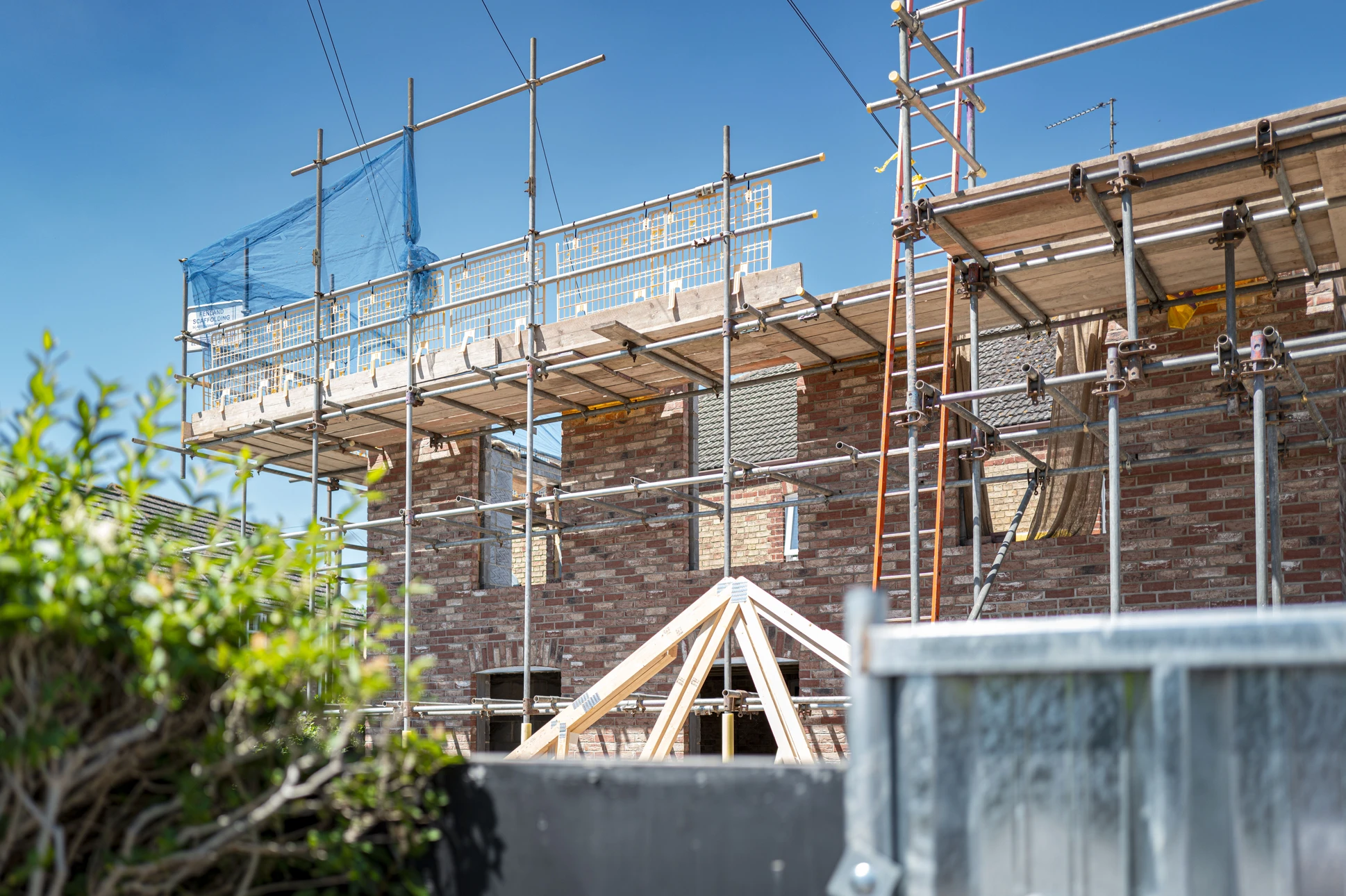 Extension de maison en construction avec murs en blocs de béton, toiture neuve en tuiles grises, échafaudage temporaire
