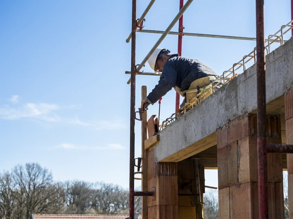 Chantier extérieur de construction avec ouvrier en casque orange appliquant du béton frais sur dalle armée