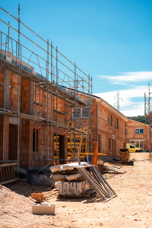 Photographie d'un maçon expérimenté travaillant sur un chantier de prestige. L'image montre un artisan en tenue professionnelle (vêtements de chantier, gilet de sécurité) effectuant des travaux de maçonnerie de qualité sur une structure de bâtiment en cours de construction. On distingue clairement du travail de gros œuvre : pose de pierre, maçonnerie fine ou préparation de fondations solides. L'arrière-plan montre un chantier professionnel et bien organisé. L'image doit transmettre l'expérience, la précision et la maîtrise de l'artisan dans son domaine.